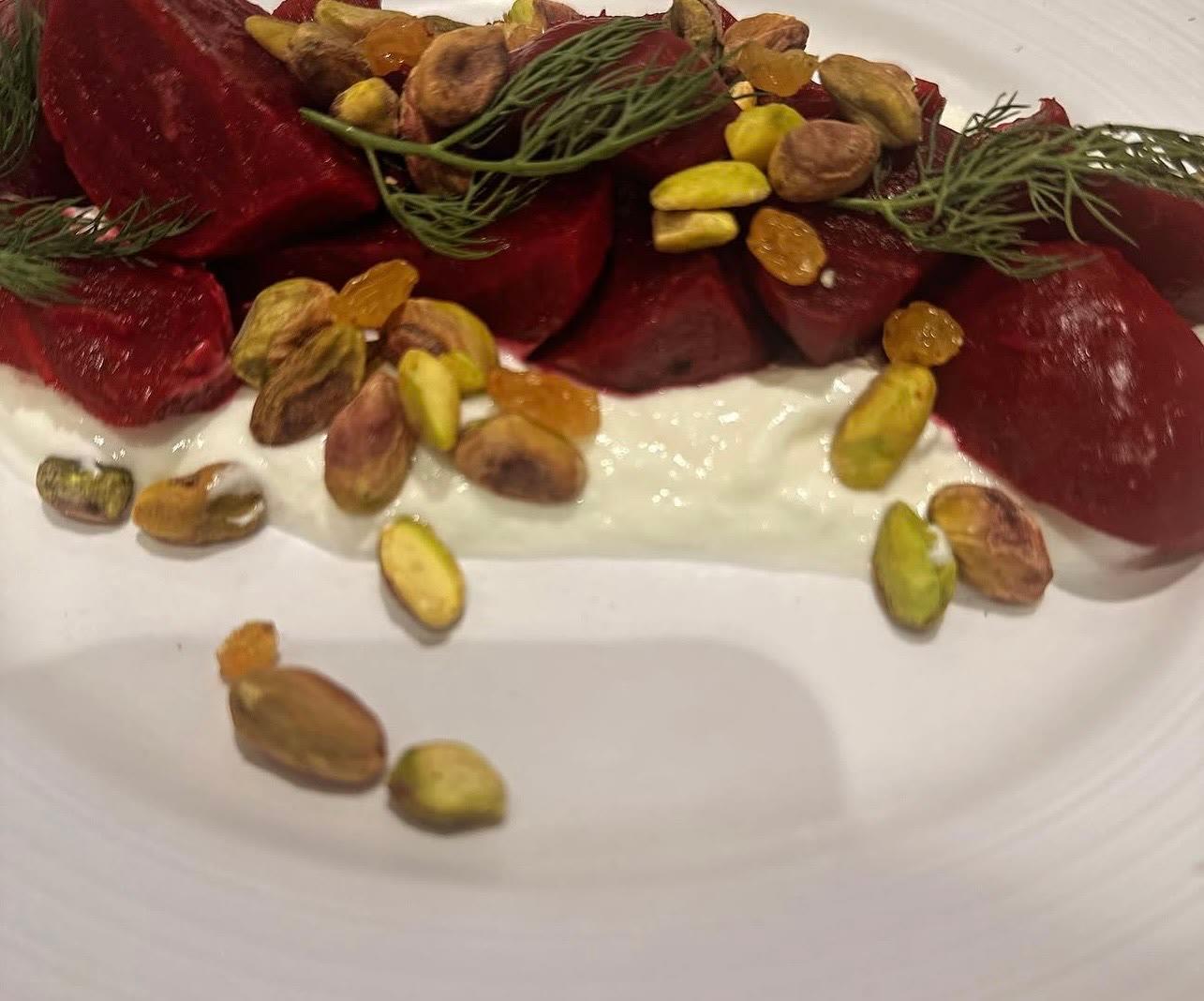 Sliced beets over a white cream with pistachios, golden raisins and fresh dill