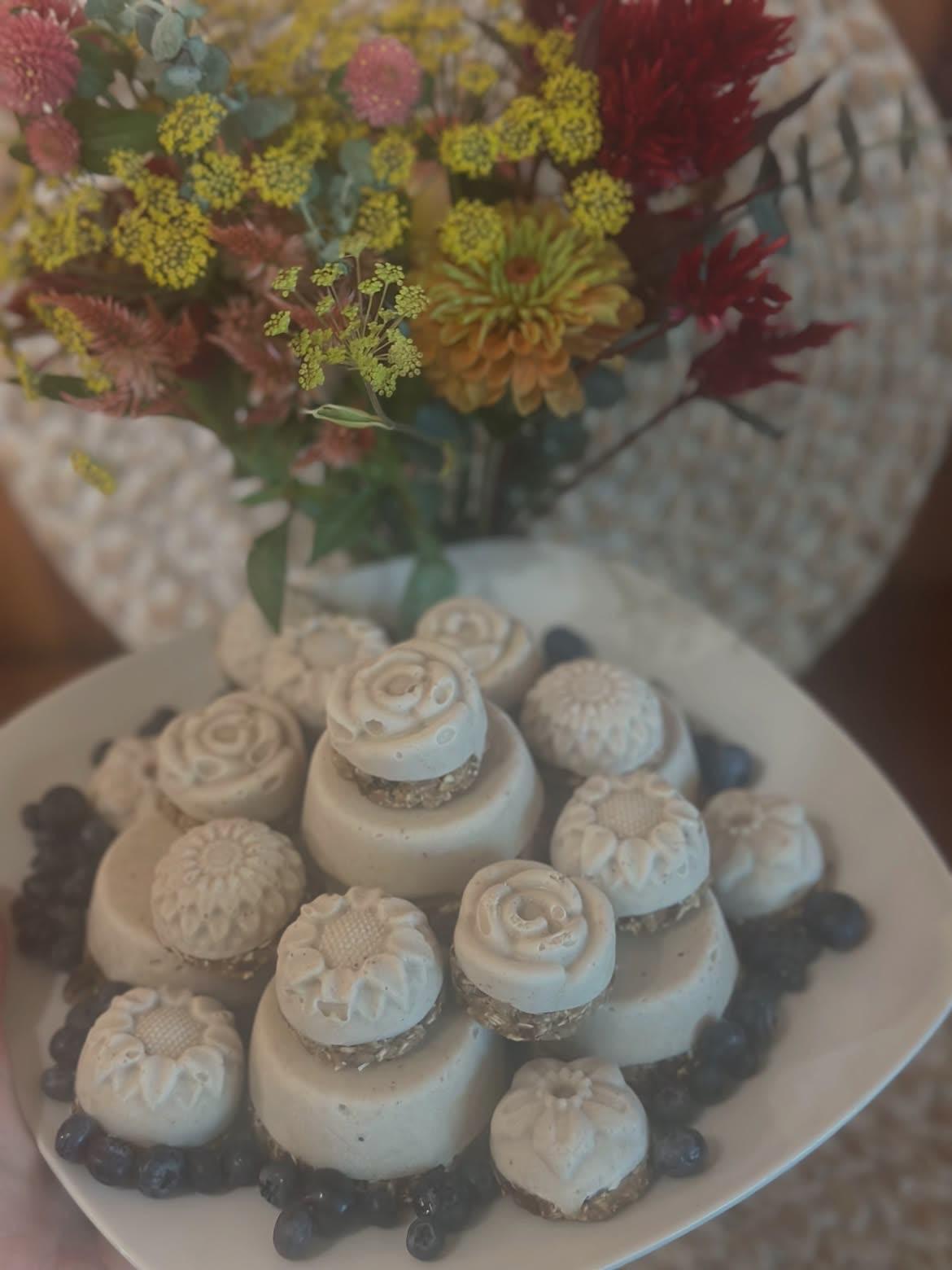 Flower-shaped desserts on a plate with blueberries beside a vase of fresh flowers